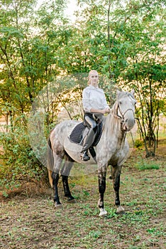 Beautiful young girl with light hair in uniform competition smiling and astride a horse in sunset