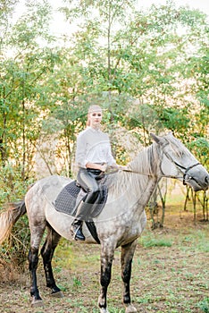 Beautiful young girl with light hair in uniform competition smiling and astride a horse in sunset