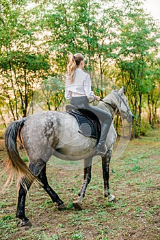 Beautiful young girl with light hair in uniform competition smiling and astride a horse in sunset