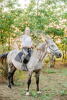 Beautiful young girl with light hair in uniform competition smiling and astride a horse in sunset