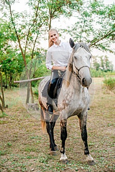 Beautiful young girl with light hair in uniform competition smiling and astride a horse in sunset