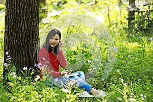 Beautiful young girl Listen to music on a mobile phone while sitting under giant oak