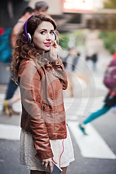 Beautiful young girl listening to music with headphones in the city