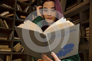 Beautiful young girl with long hair reads a book in the library