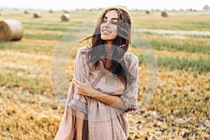 Beautiful young girl with long hair in sunnglasses and straw hat posing on a wheat field near hay bales. Happy brunette in summer