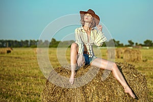 Beautiful young girl with long thin legs and naked belly in a cowboy hat and denim shorts on the yellow field poses