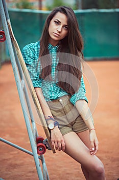 Beautiful young girl with longboard standing on the tennis court