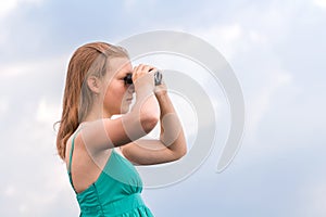 Beautiful young girl looking through binoculars at sea at sunrise in cloudy weather