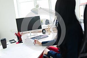 Beautiful young girl is looking through documents, sitting in the office at the table.