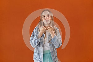 A beautiful young girl looks at the camera and blows a kiss. Orange background.