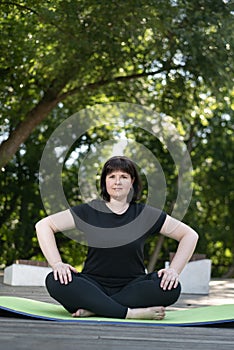 Beautiful young girl meditates in the park sitting on a green yoga mat. Healthy lifestyle. Lotus position