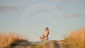 Beautiful young girl meditating on the hill in the rays of the setting sun