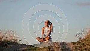 Beautiful young girl meditating on the hill in the rays of the setting sun
