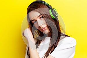 Beautiful young girl model listens to music in headphones on a yellow background