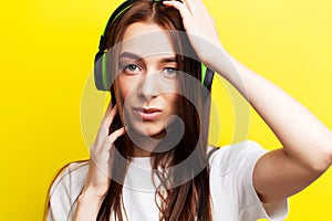 Beautiful young girl model listens to music in headphones on a yellow background