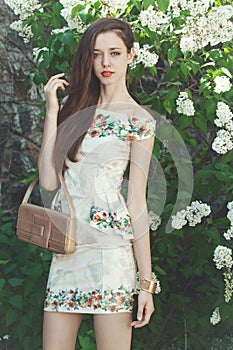 Beautiful young girl model posing near blooming lilacs at spring