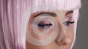 Beautiful young girl model posing in a pink short bob wig, rhinestones on her eyes and stylish pink makeup, high fashion