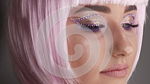 Beautiful young girl model posing in a pink short bob wig, rhinestones on her eyes and stylish pink makeup, high fashion