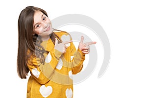 Beautiful young girl in mustard yellow sweater looking at camera, smiling and pointing to the side. Waist up studio shot.