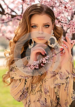 Beautiful young girl with natural hair color in elegant clothes posing among flowering peach trees