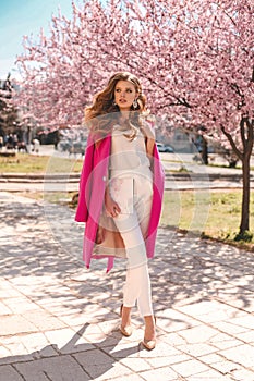 Beautiful young girl with natural hair color in elegant clothes posing among flowering peach trees
