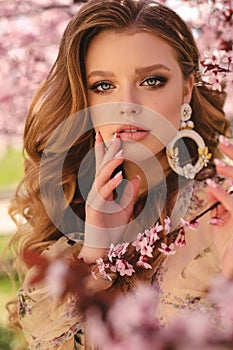 Beautiful young girl with natural hair color in elegant clothes posing among flowering peach trees