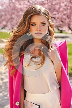 Beautiful young girl with natural hair color in elegant clothes posing among flowering peach trees