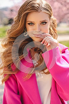 Beautiful young girl with natural hair color in elegant clothes posing among flowering peach trees