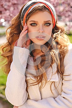 Beautiful young girl with natural hair color in elegant clothes posing among flowering peach trees