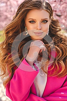 Beautiful young girl with natural hair color in elegant clothes posing among flowering peach trees