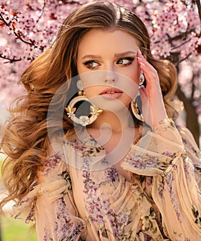 Beautiful young girl with natural hair color in elegant clothes posing among flowering peach trees