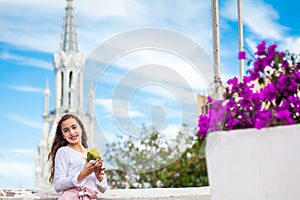 Beautiful young girl on the Ortiz Bridge eating a mango. On background the famous gothic church of La Ermita built on 1602 in the photo