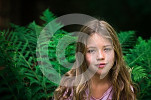 Beautiful young girl with perfect natural skin posing in front of plants background with fern, kid model with brown hair taking