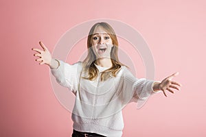 Beautiful young girl on a pink background in the studio stretches out her arms for a hug.