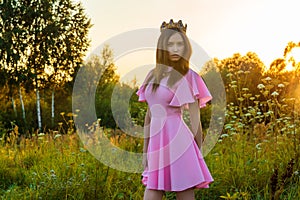 Beautiful young girl in pink dress with crown on head at sunset