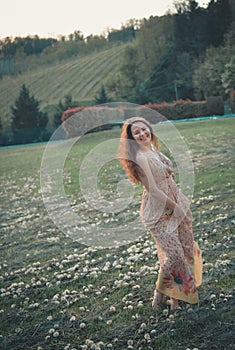 Beautiful young girl playing in dandelion field in beautiful spring warm sunset