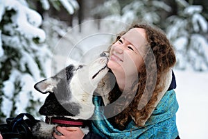 Beautiful young girl playing with a dog on a Sunny winter day. The dog licks her face. Tenderness. Friendship