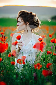 Beautiful young girl in poppy fields at sunset.