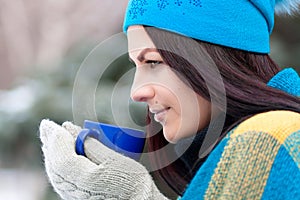 Beautiful young girl portrait on winter background. A charming young lady walking in a winter forest. Attractive woman with Cup.