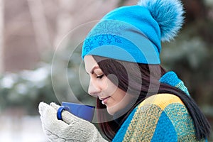 Beautiful young girl portrait on winter background. A charming young lady walking in a winter forest. Attractive woman with Cup.