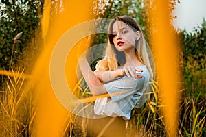 Beautiful young girl posing against high grass in early warm autumn