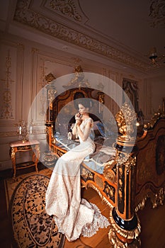 A beautiful young girl in a powdery wedding dress on the background of the interiors of a luxurious historical apartment.