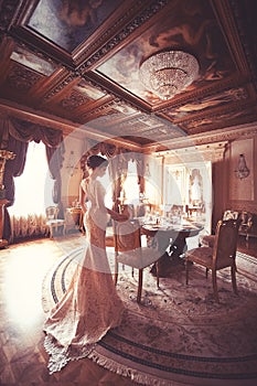 A beautiful young girl in a powdery wedding dress on the background of the interiors of a luxurious historical apartment.