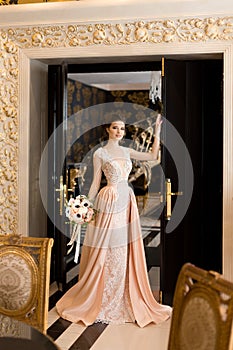 A beautiful young girl in a powdery wedding dress on the background of the interiors of a luxurious historical apartment.