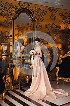 A beautiful young girl in a powdery wedding dress on the background of the interiors of a luxurious historical apartment.