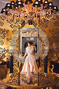 A beautiful young girl in a powdery wedding dress on the background of the interiors of a luxurious historical apartment.