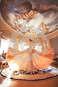 A beautiful young girl in a powdery wedding dress on the background of the interiors of a luxurious historical apartment.