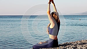 Beautiful young girl practicing yoga, relaxing sitting in yoga lotus pose on the beach at the seaside at the sunrise