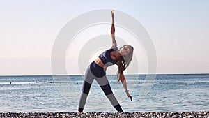 Beautiful young girl practicing yoga, stretching on the beach