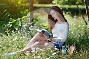 Beautiful young girl reads a book in park outdoors